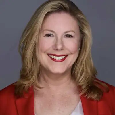Kim Farington in a red blazer, studio headshot against a grey background.